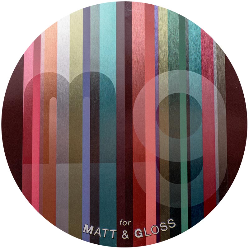 A matte gloss finish depicting a lowercase "m" and "g" faintly against a striped glossy background with lots of different neutral colors.