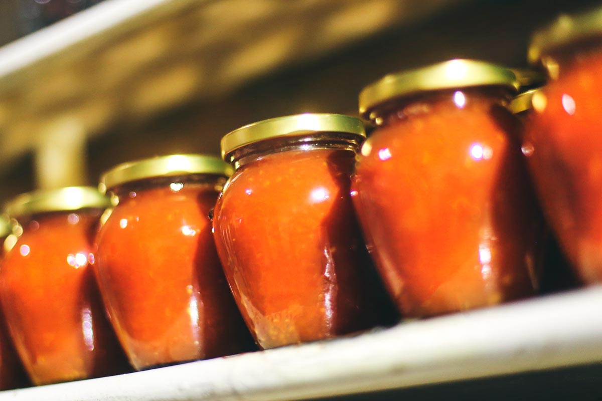 Glass jars filled with red sauce lined up on a shelf with gold lids.