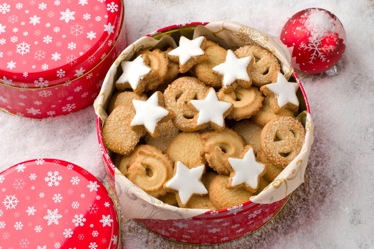 Open red holiday tin filled with assorted cookies, including star-shaped cookies with white icing.