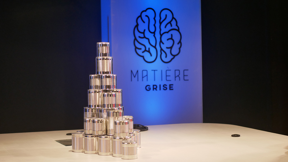 Silver cans stacked in a pyramid next to a sign that says, Matiere Grise.