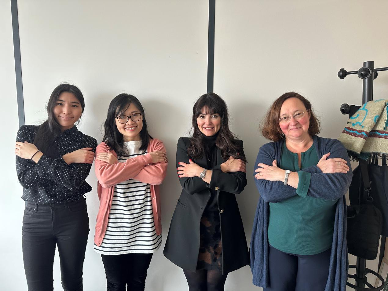 Four women stand in front of a wall with their arms crossed in the symbol for 'equity'.