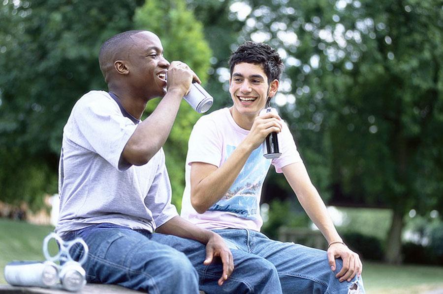 Two teenagers sitting and drinking from beverage cans