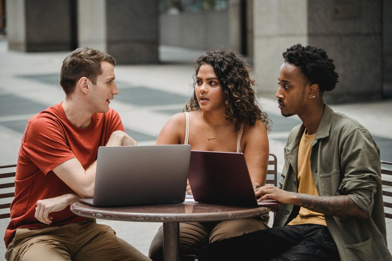 three young people having a conversation around laptops