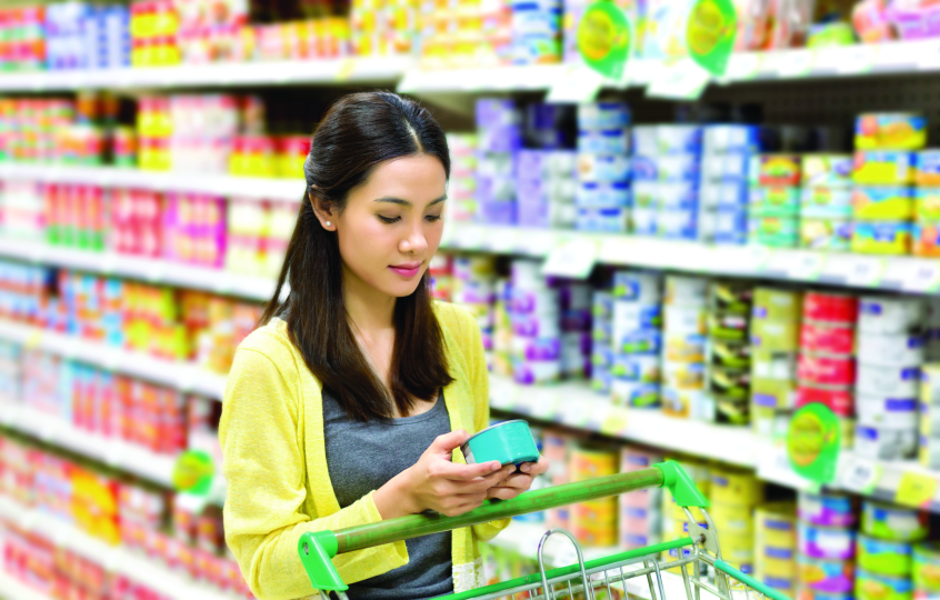 Young woman in a grocery store aisle looking at the label on a can of food