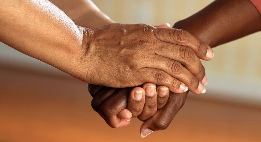 A medium-dark skinned hand holds onto another dark-skinned hand, both of whom are off screen.