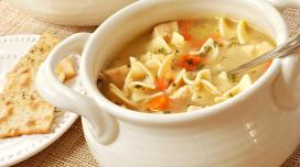 A fancy bowl holding a large serving of soup sits next to a plate of saltine crackers.