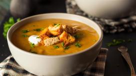 A bowl of soup with several croutons sitting on a flannel placemat.