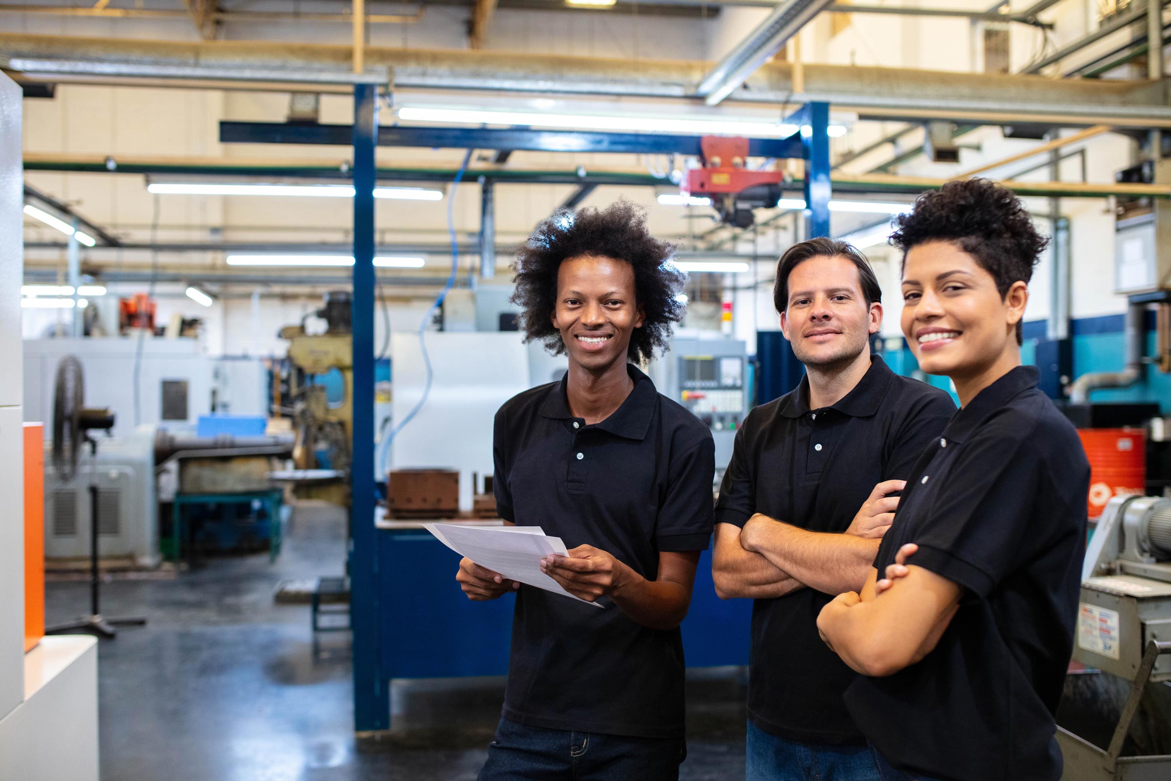 A diverse group of 3 workers in polo shirts in a factory setting