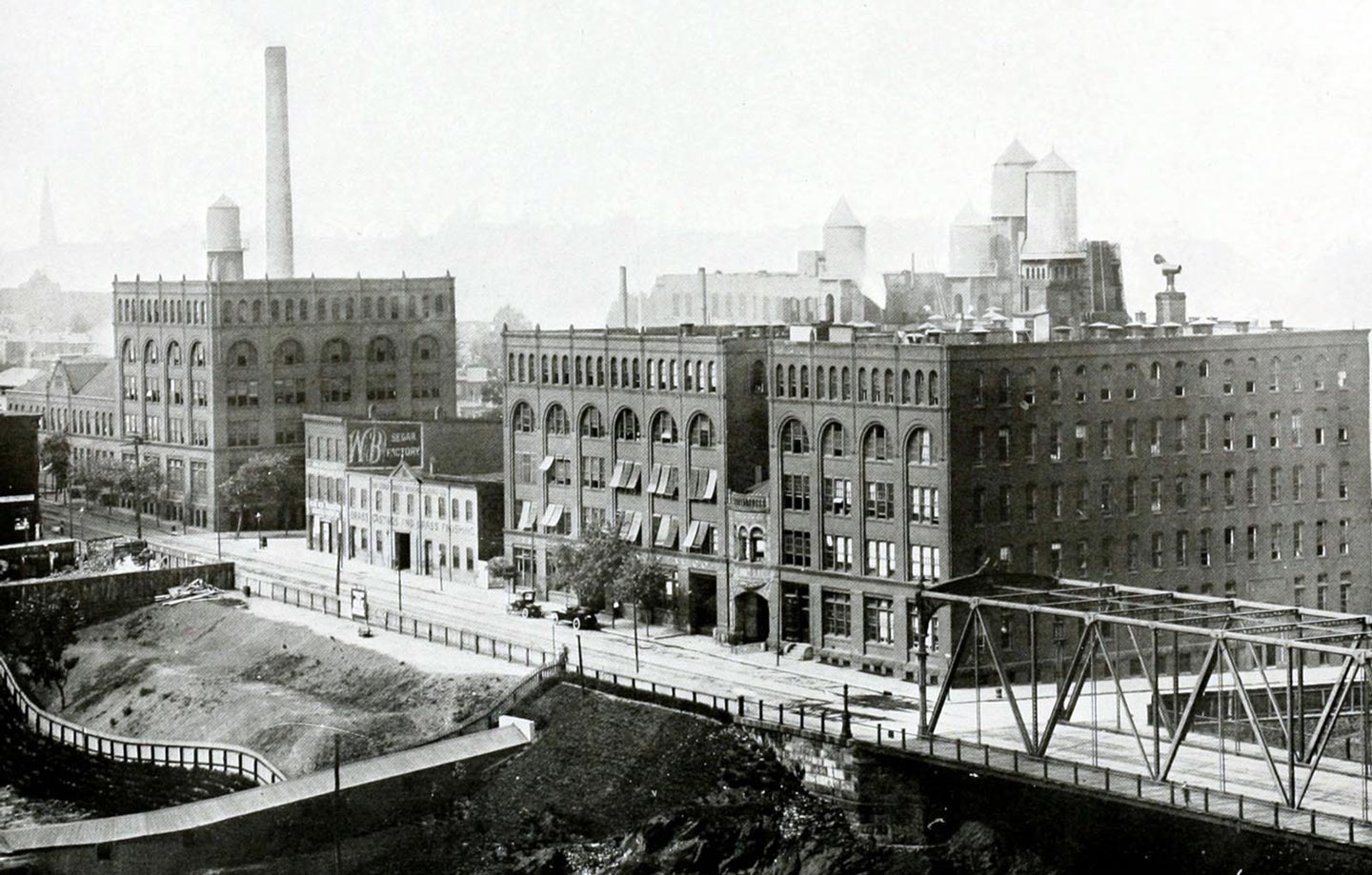 Black and white photo of a brick factory with train tracks in front of it