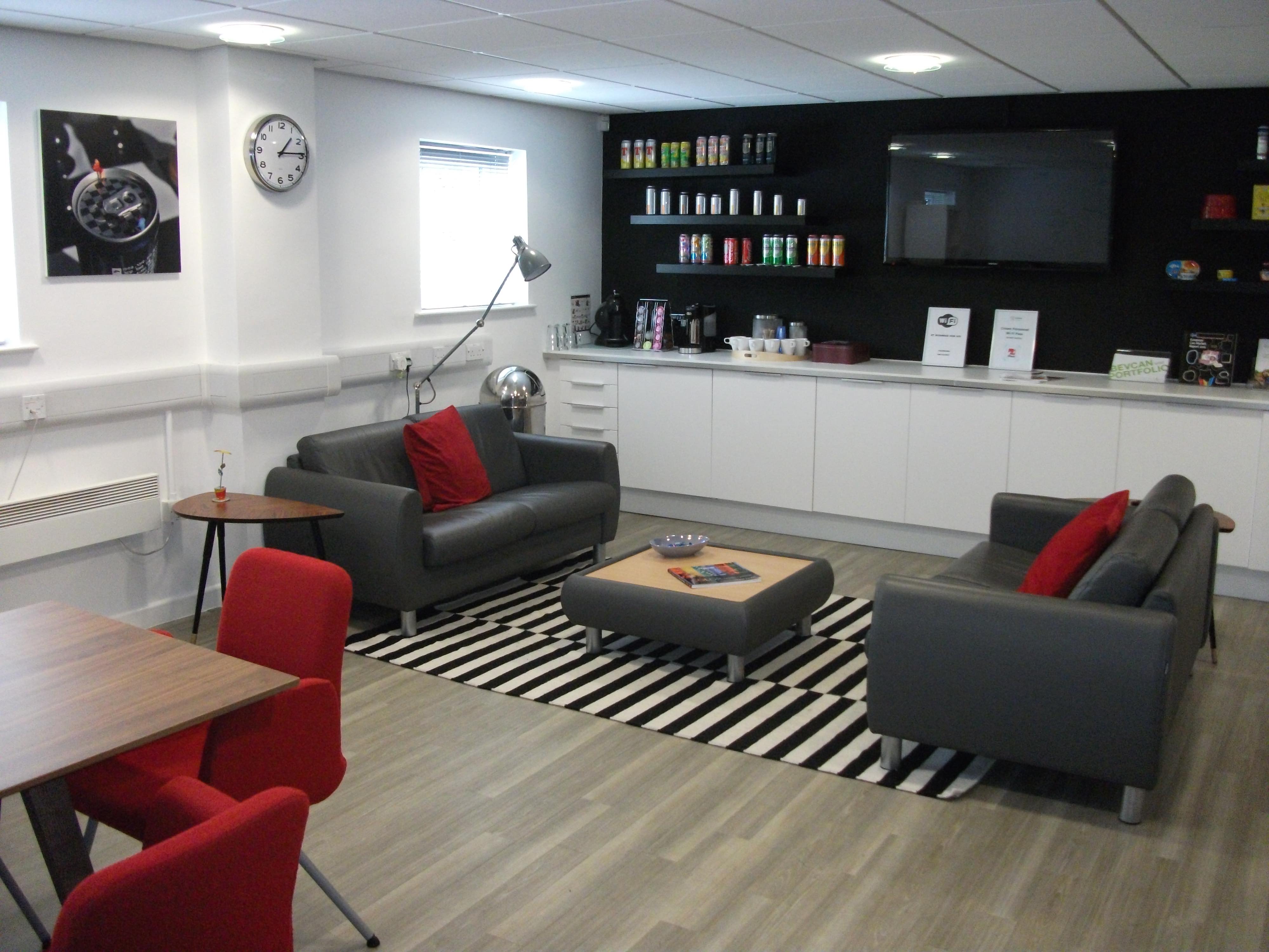Area for customers containing two grey couches, a can display area, and table with red chairs.