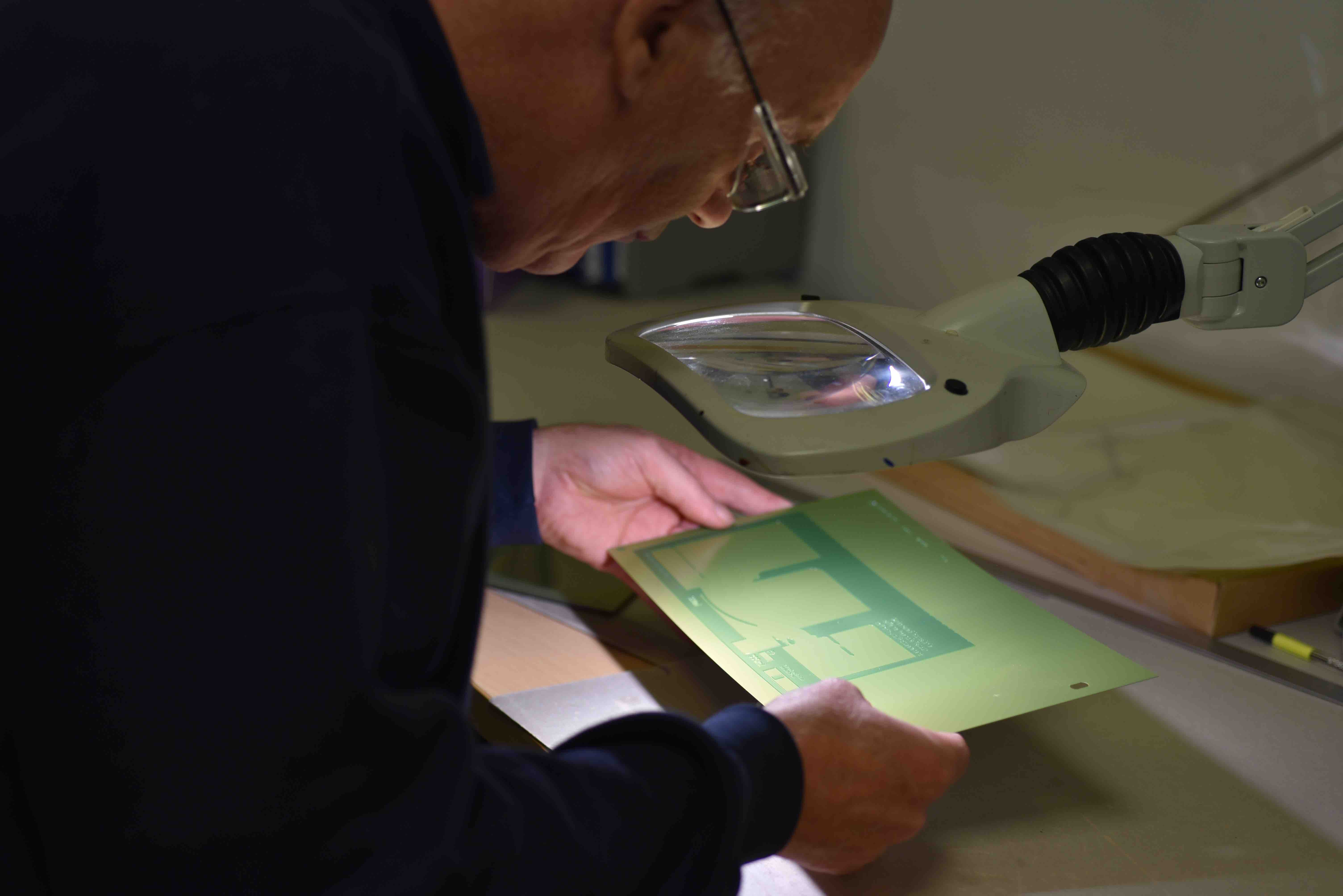 Man bent over a magnifying glass looking at a graphic to convert into a can compatible design