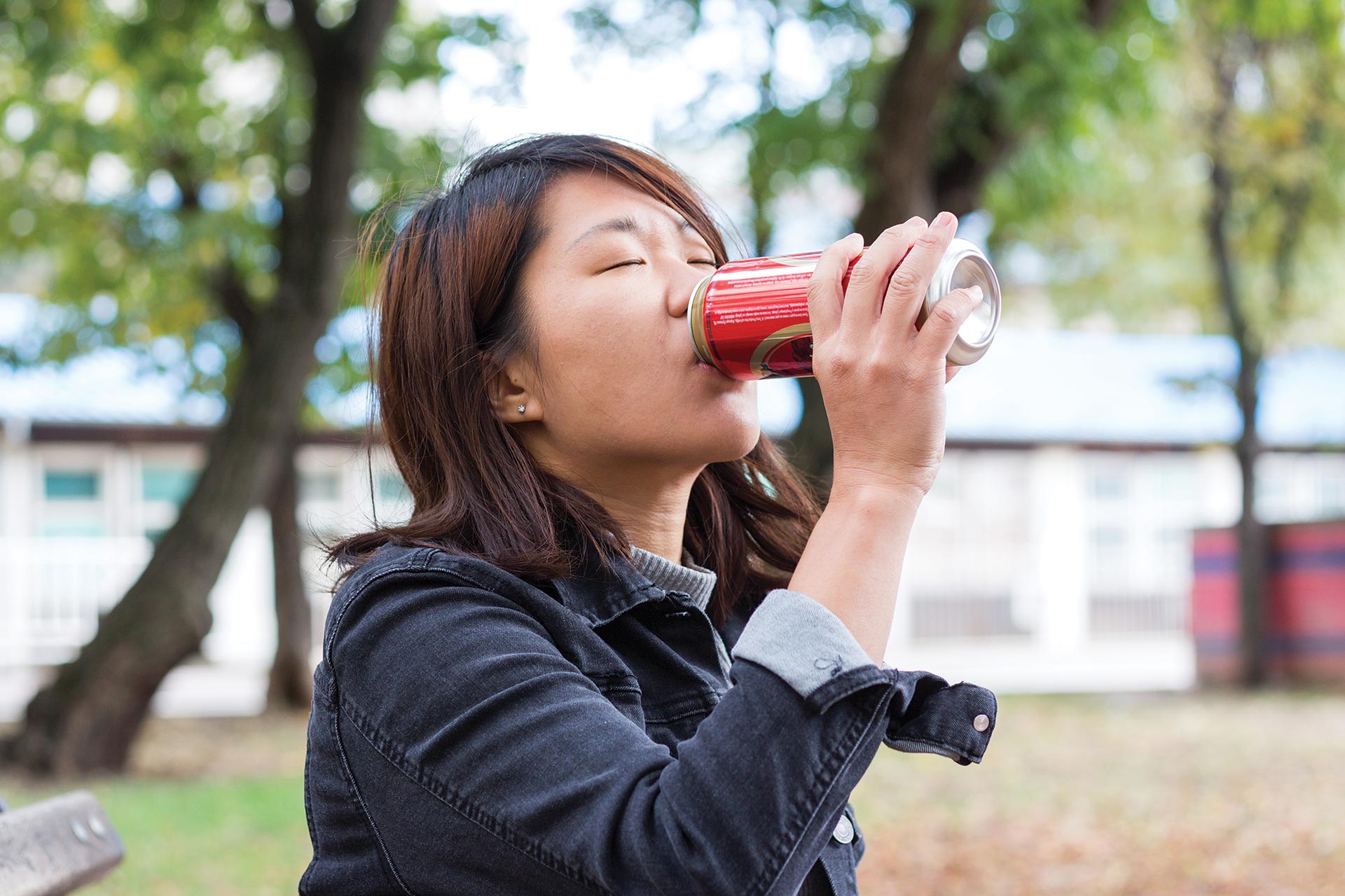 A female-presenting person drinks an energy drink outdoors.