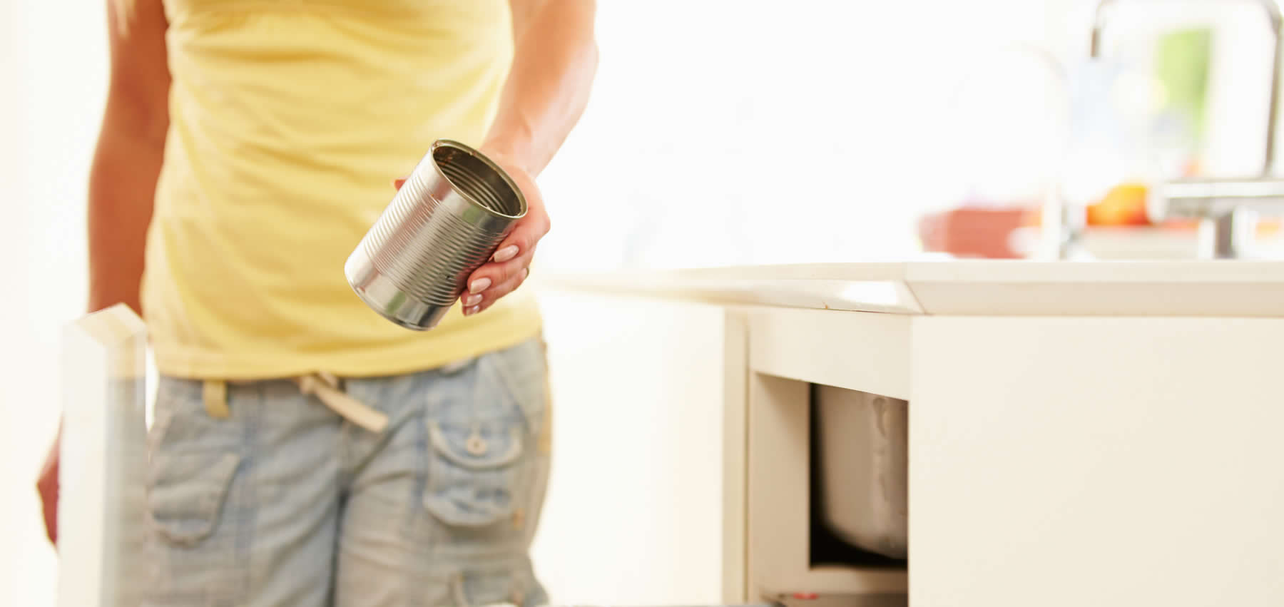 A person out of frame holds an empty aluminum food can in a kitchen.
