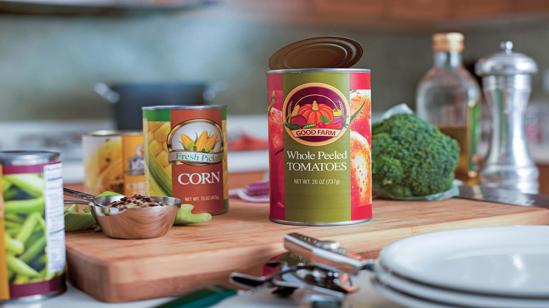 Several opened steel food cans sit on a cutting board in a kitchen.
