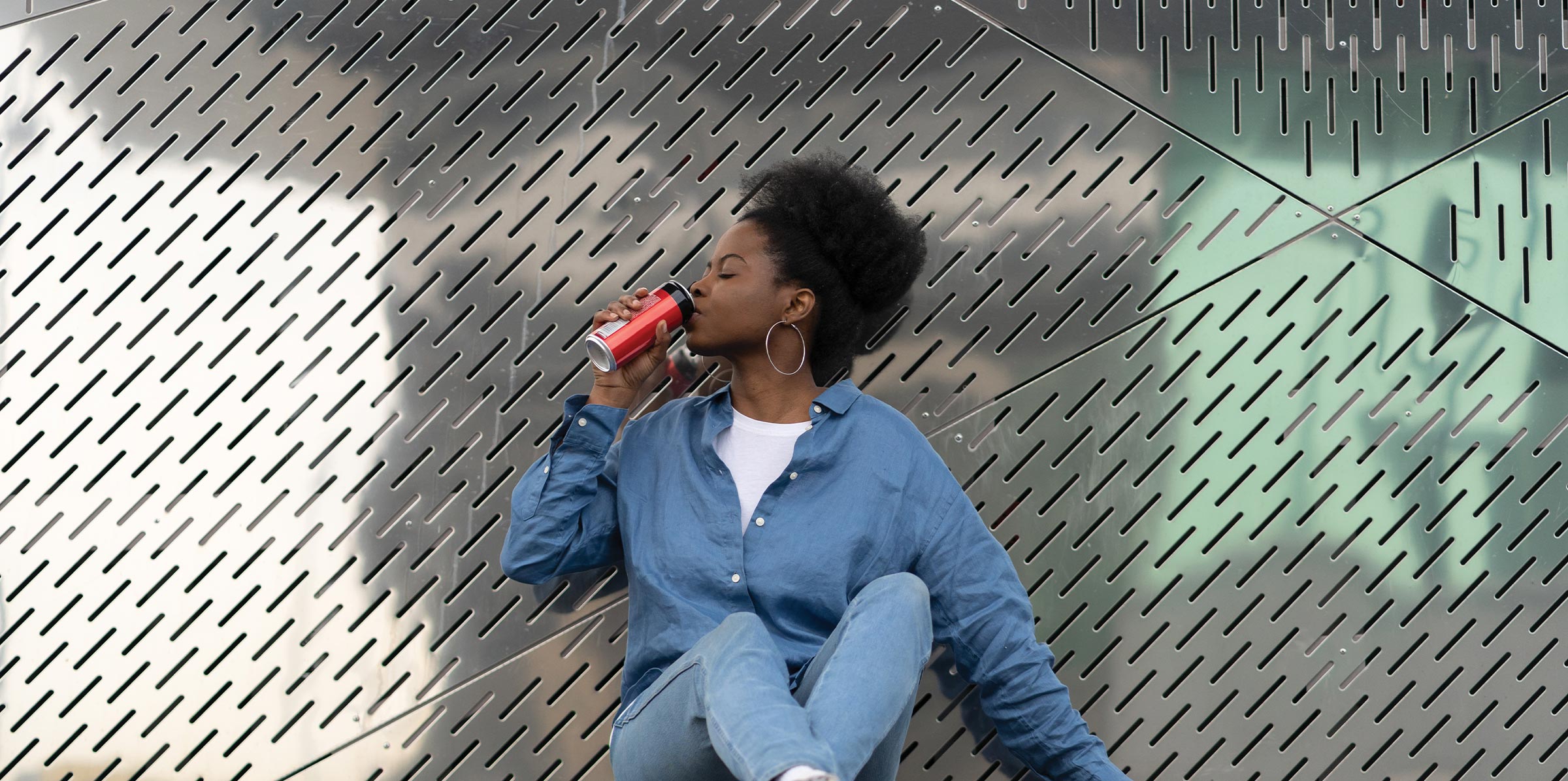 African skateboarder girl refreshing after longboarding sit on skate drinking soda beverage from metal can. Trendy urban young female relaxing after active training on longboard in urban space