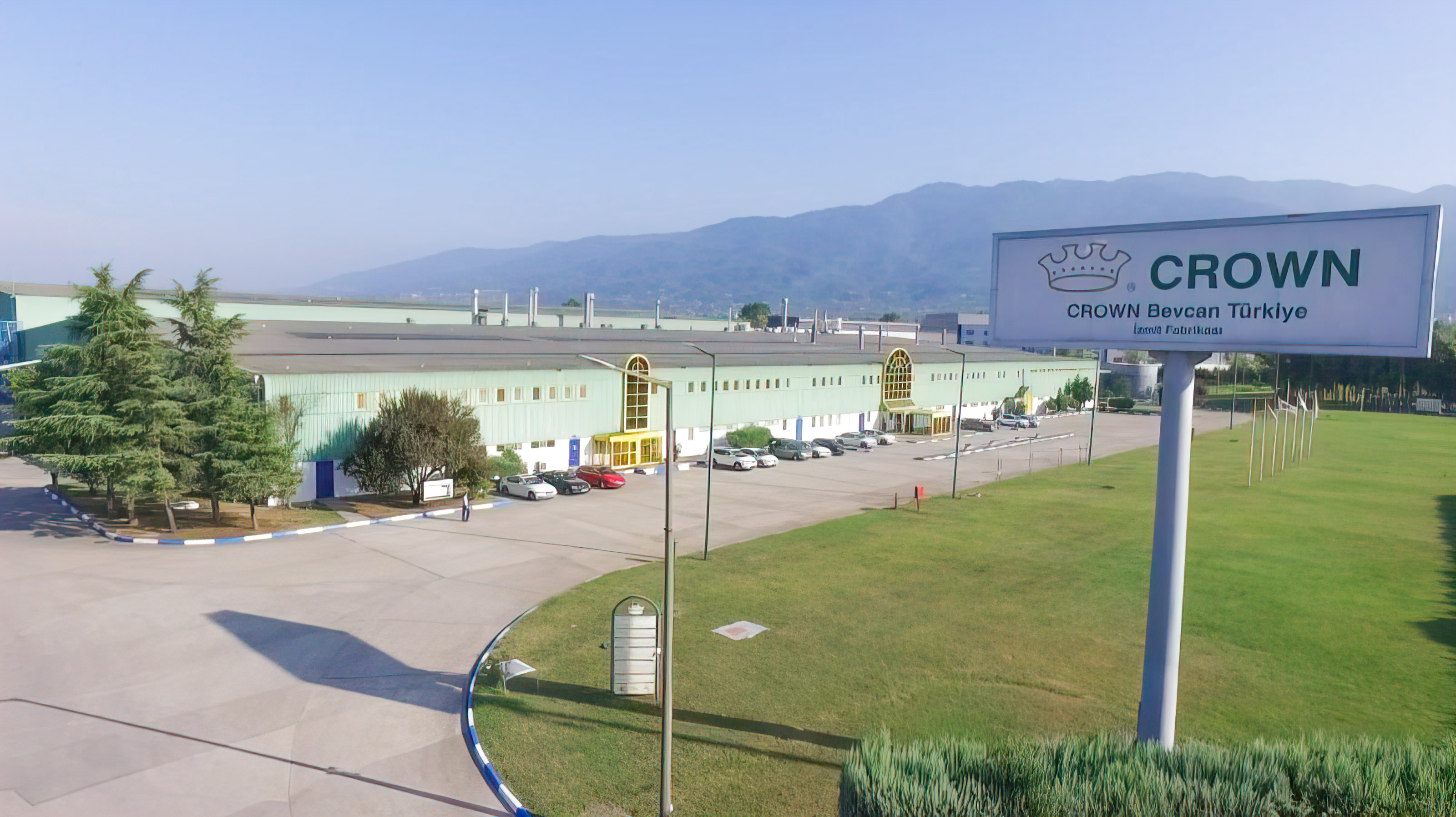 Manufacturing plant with sign that says Crown Bevcan Turkiye with mountains