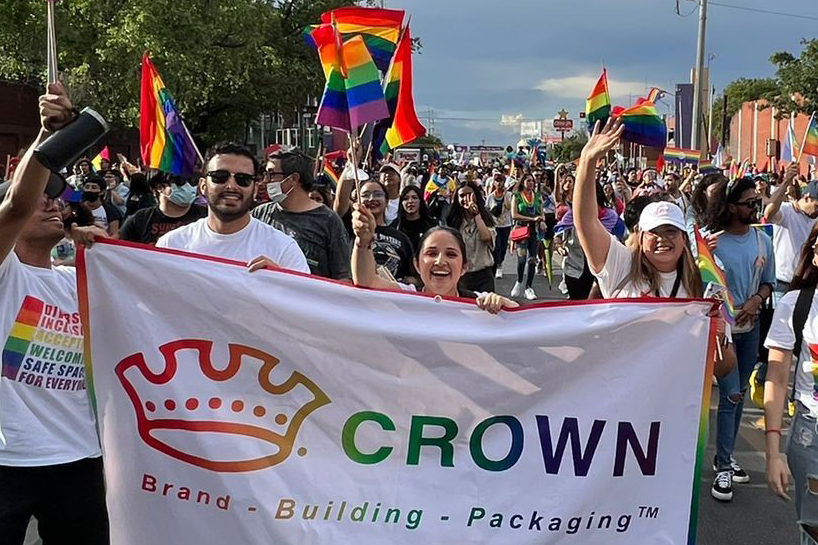 People holding a rainbow version of the Crown logo on a flag marching in a pride parade in Mexico