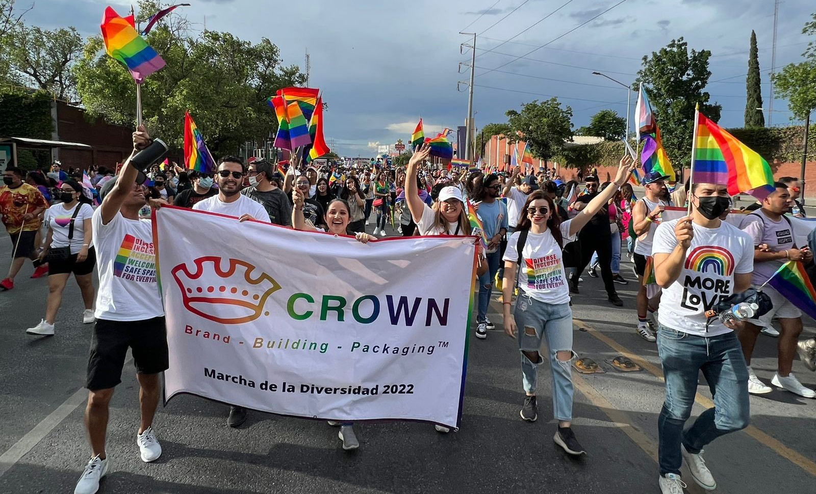 A group of people holding a rainbow Crown logo banner in a pride parade