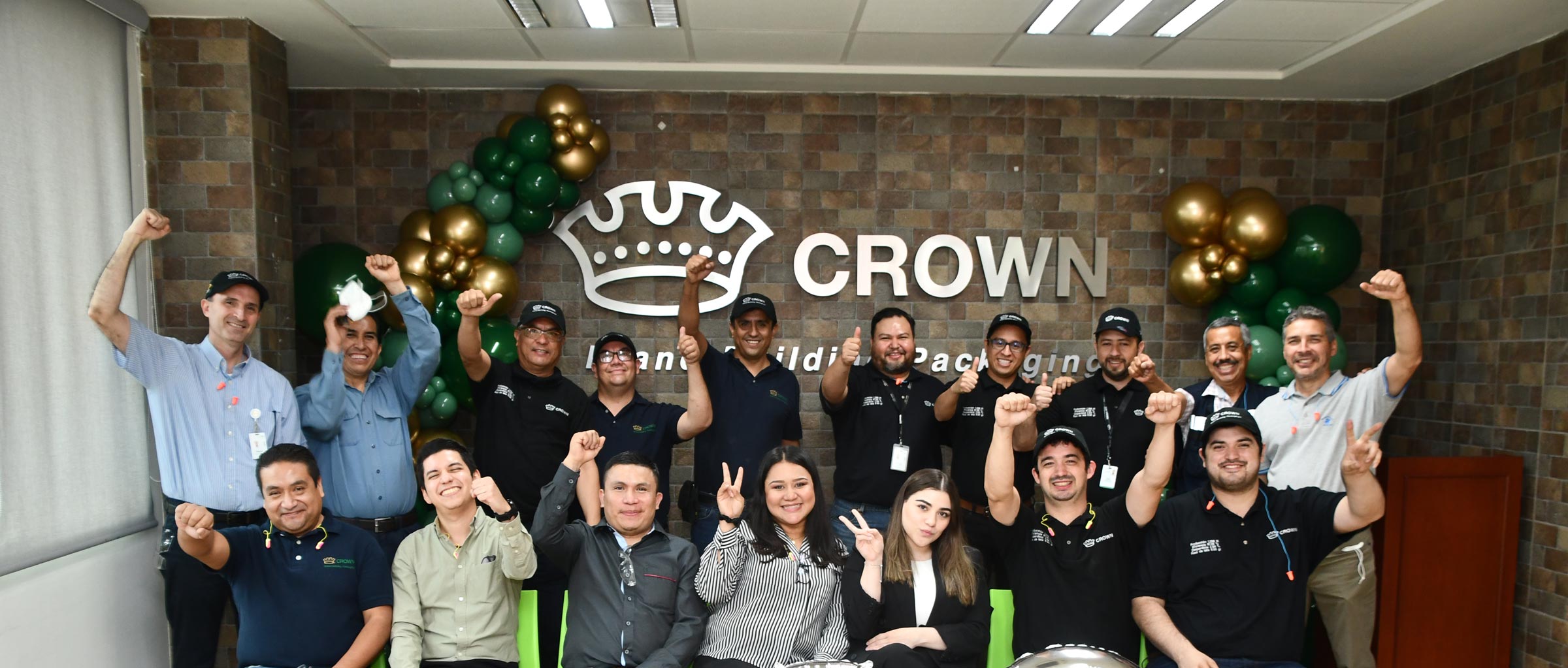 A group of Crown employees in jeans and collared shirts posing for a picture in front of a Crown sign.