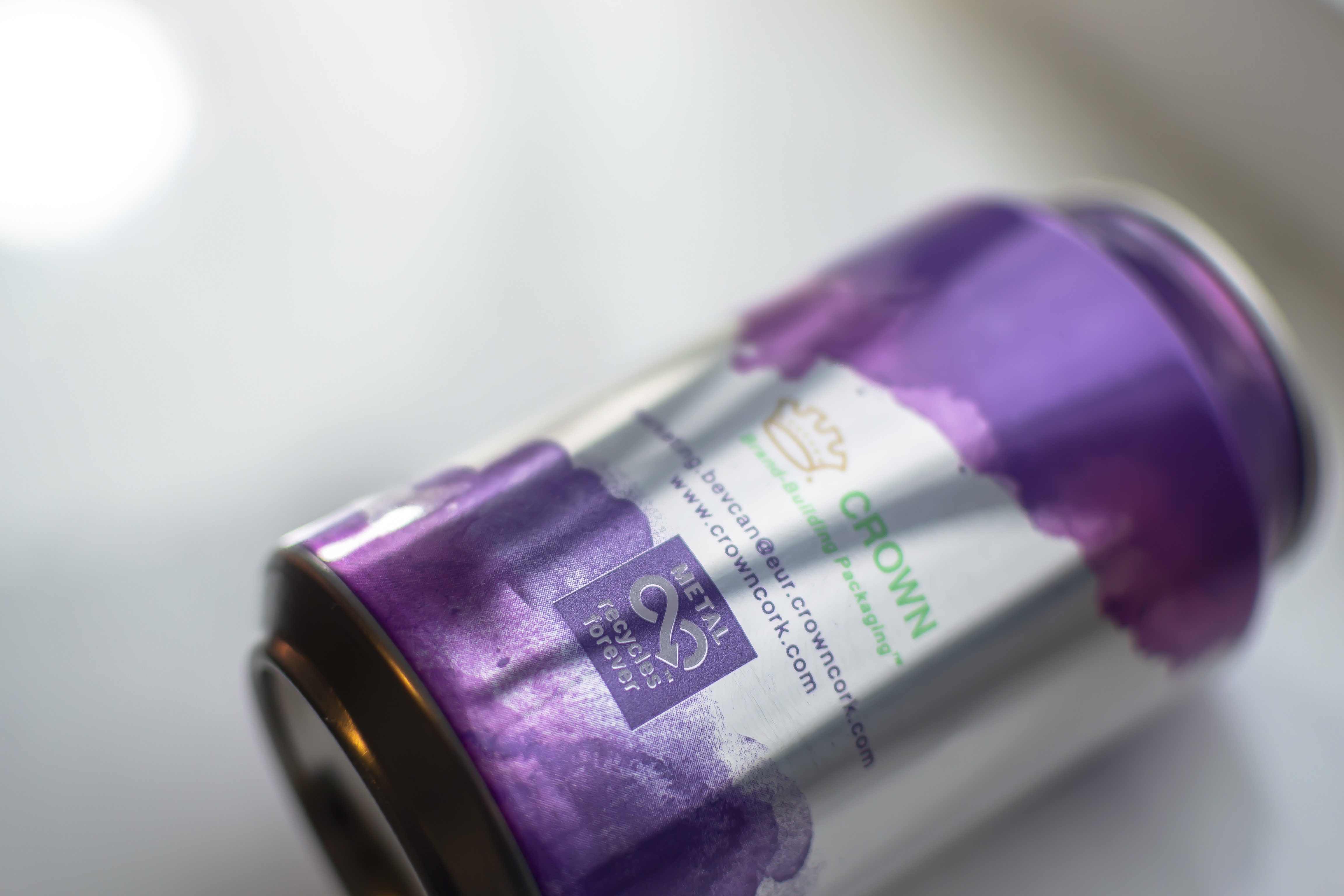 Crown to Reinforce Its Commitment to Sustainability at Drinktec 2022 A Crown aluminum can with purple watercolor on the top and bottom lays against a white background. It says "metal recycles forever" on the side.
