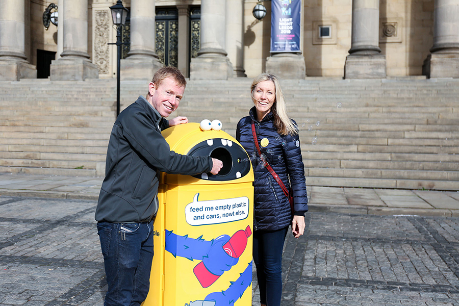 Two people standing next to a yellow garbage can.