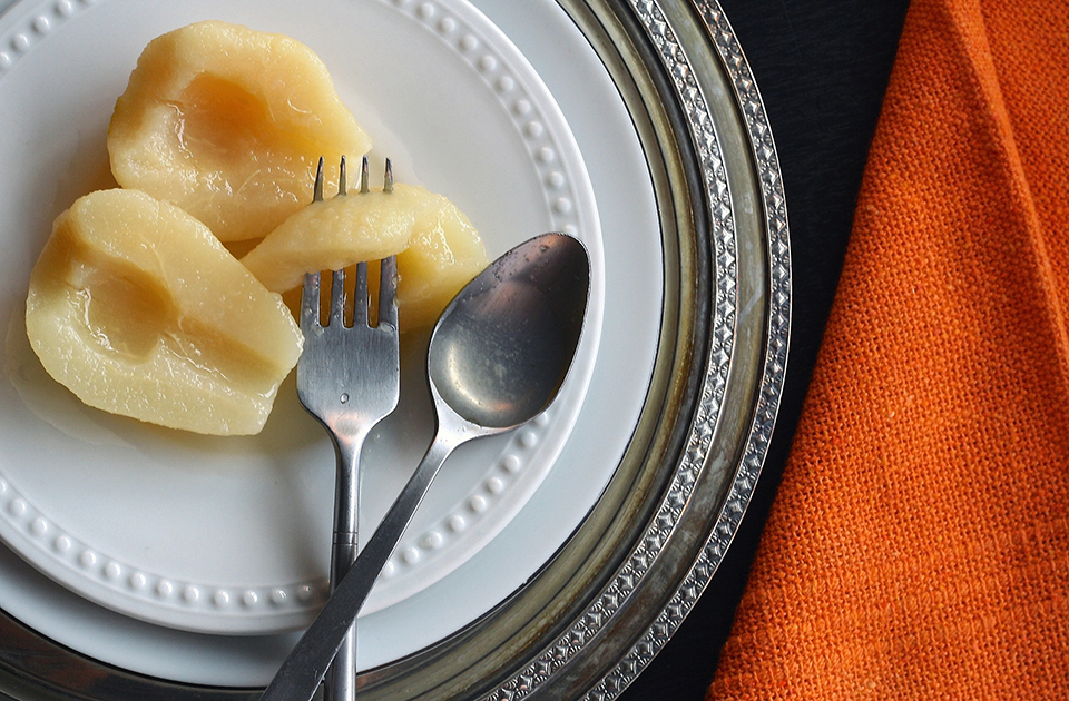 Sliced pears on a white plate with a fork and spoon next it them.