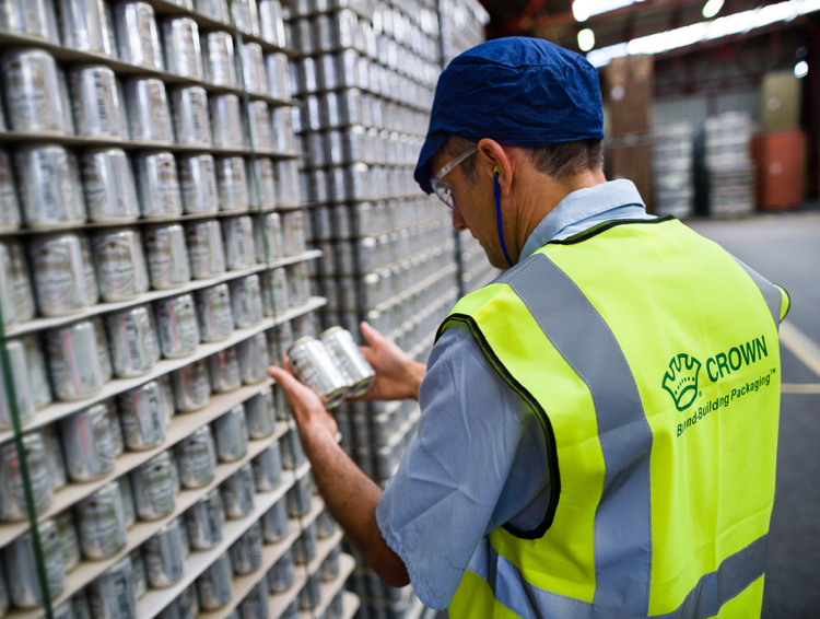A warehouse worker in a high-visibility vest inspecting aluminum beverage cans.