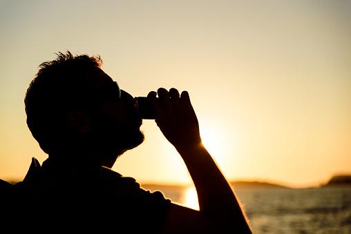 Person drinking from a can in front of a sunset