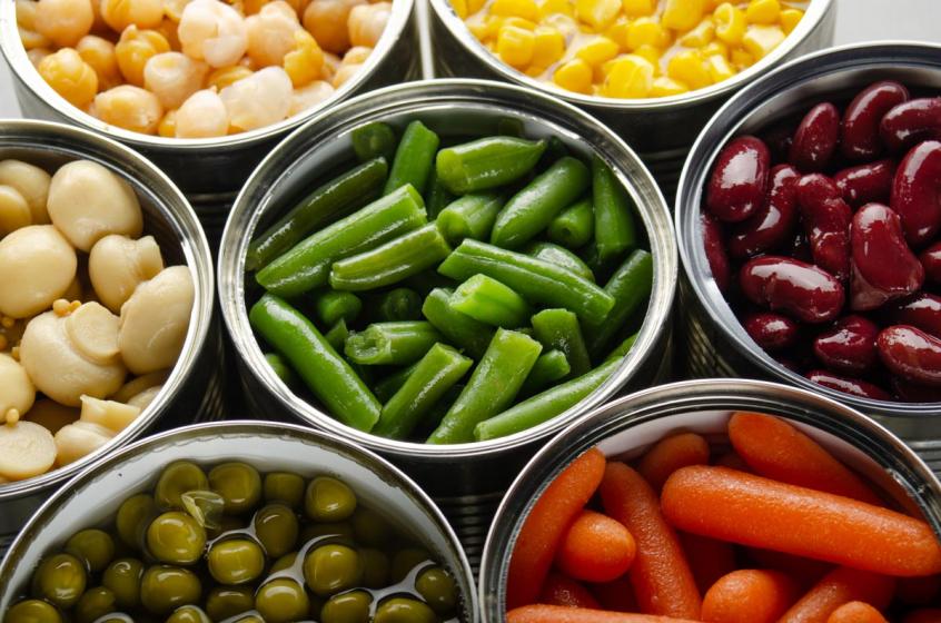 Canned vegetables in opened tin cans on kitchen table. Non-perishable long shelf life foods background