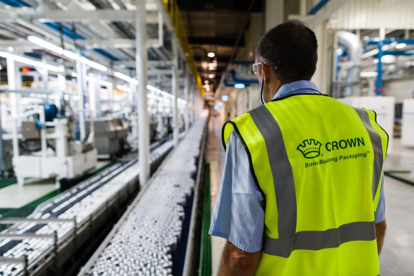 Man in safety vest in plant where aluminum cans are on conveyor belt