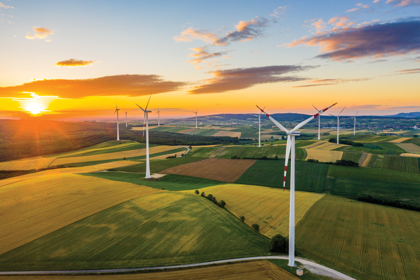 A landscape with several wind turbines in farm fields as the sun sets in the background.