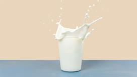 A tall glass of milk splashes, as if something has been dropped into the class directly from above.