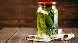 A mason jar of pickles sits on top of a tan placemat on a rustic wooden table.