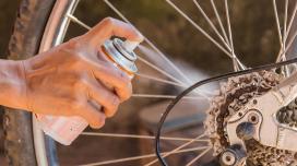 A person out-of-frame sprays an aerosol can onto the gears of a bicycle wheel.